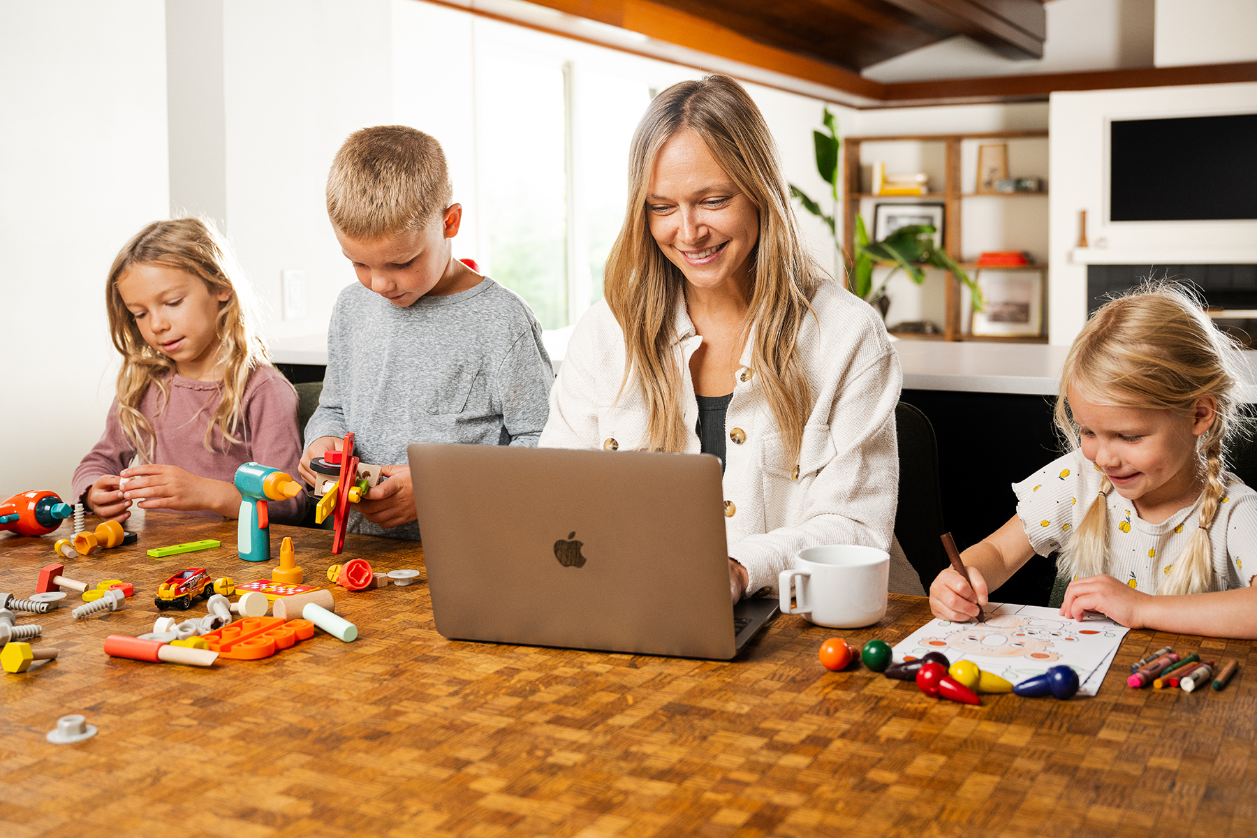 A parent working at a laptop while children create at the table